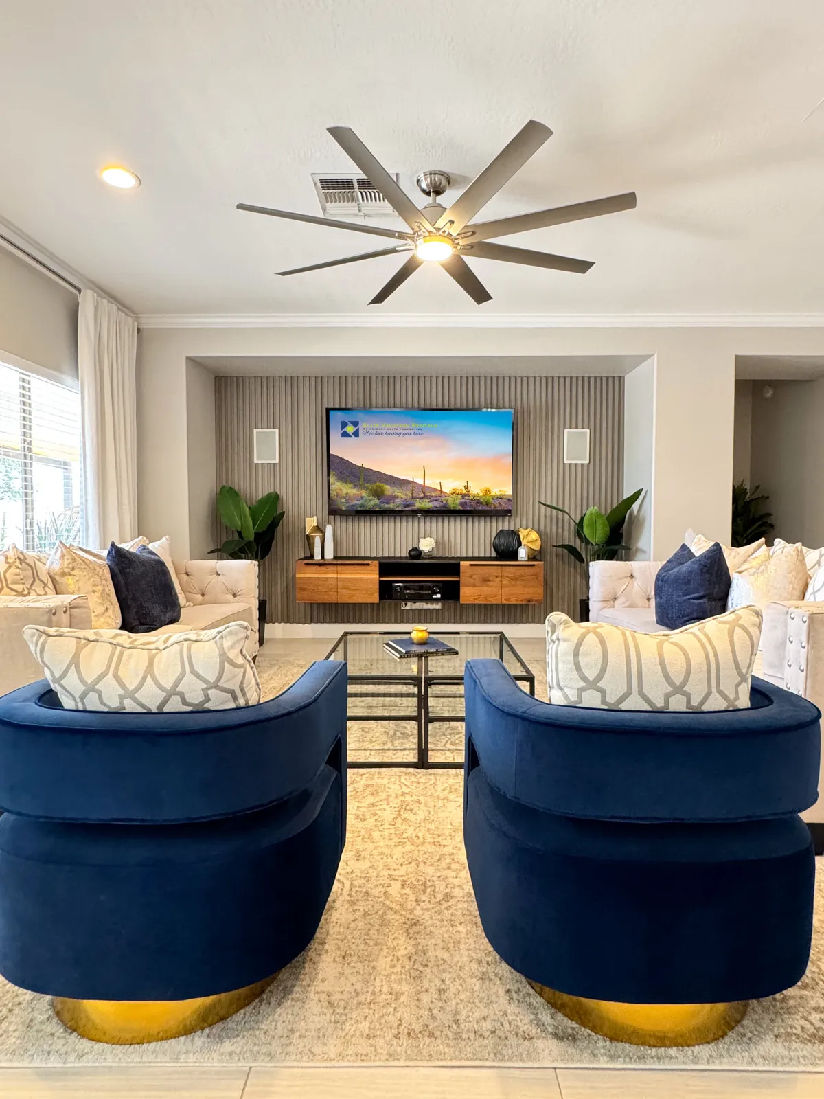 A stylish and comfortable movie room setup featuring blue swivel chairs, a modern TV, and a wooden media console. The seating is oriented for optimal viewing, providing a cinema-like vibe for movie nights.