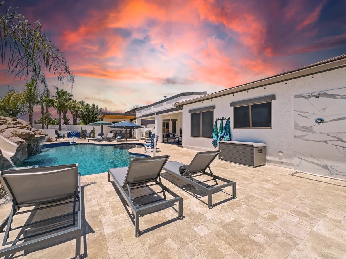 A vibrant poolside scene with a clear swimming pool, colorful towels hanging from loungers, lush palm trees, and an inviting outdoor seating area. The atmosphere is leisurely and cheerful, reflecting a perfect summer day for families.