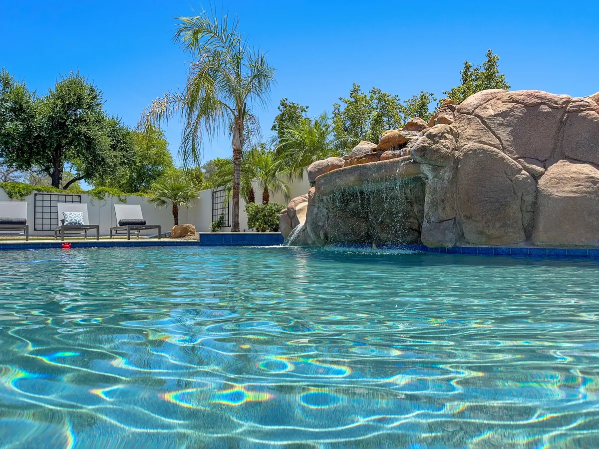 This image showcases a sparkling pool surrounded by palm trees and lounge chairs, creating a relaxing and resort-like atmosphere. The tranquil water, lush greenery, and open sky evoke a sense of leisure and rejuvenation.