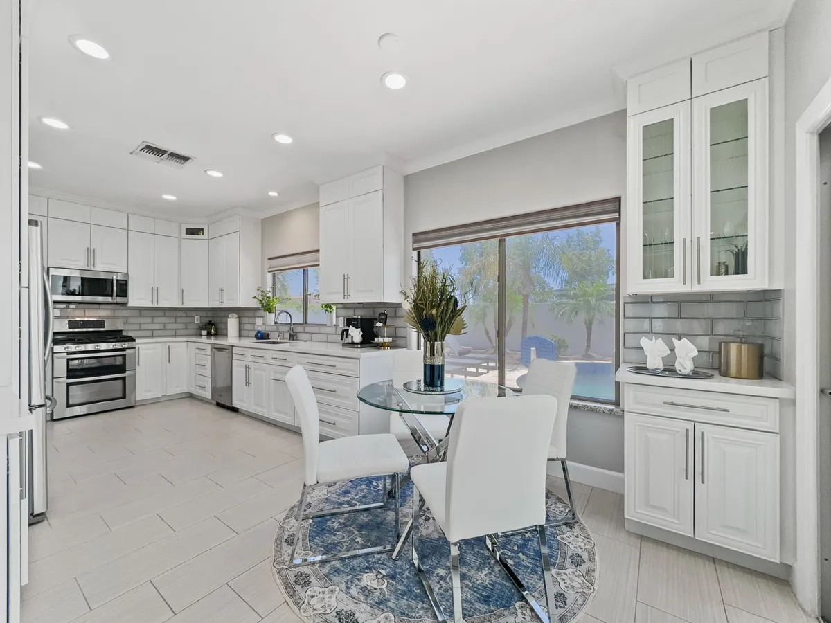 An inviting kitchen and dining area featuring a central kitchen island, a round dining table, and large windows that flood the space with natural light. The decor is modern and warm, emphasizing comfort while offering views into the surrounding space.