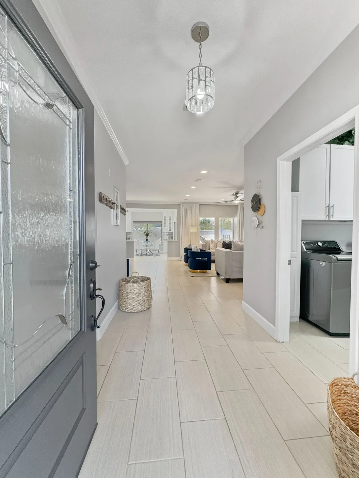 A welcoming interior scene highlighting the front door, a modern chandelier, cozy living room seating, and a visible laundry room with woven baskets. The layout suggests comfort, functionality, and thoughtful design for everyday living and extended stays.