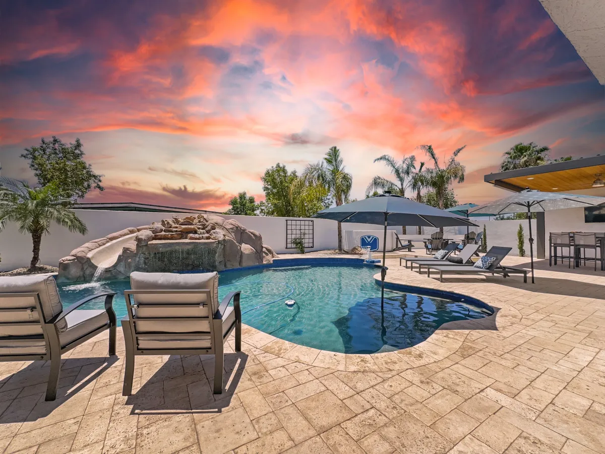 A luxurious pool scene featuring a waterfall, multiple lounge chairs, umbrellas, and an outdoor seating area. The expansive outdoor space is designed for both relaxation and social gatherings, with the waterfall feature adding a touch of luxury.