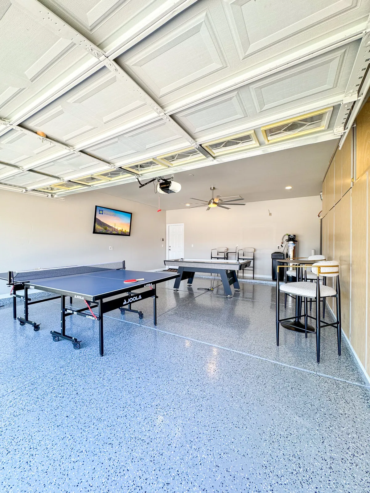 A lively game room centered around a ping pong table, complete with bar stools and a TV screen. The space is casual and inviting, perfect for games, friendly competition, and socializing.